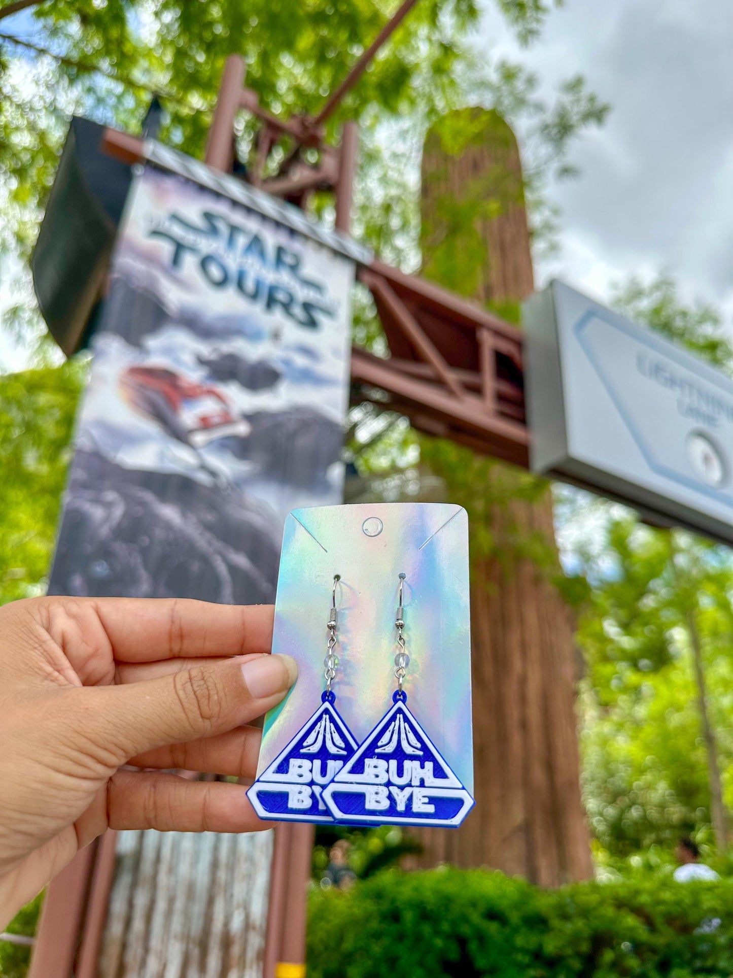 May include: A pair of blue and white earrings with the words &#39;BUH BYE&#39; on them. The earrings are hanging from a silver hook.